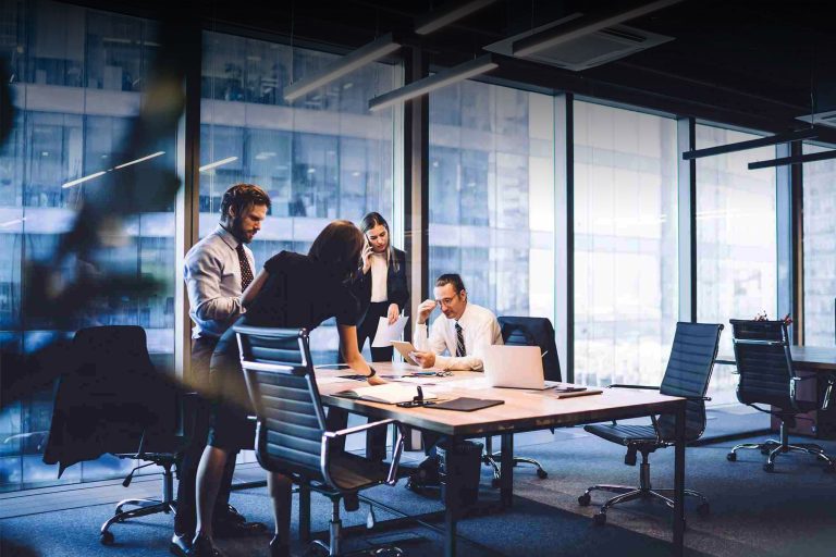 Four colleagues working around a boardroom table beside floor-to-ceiling windows