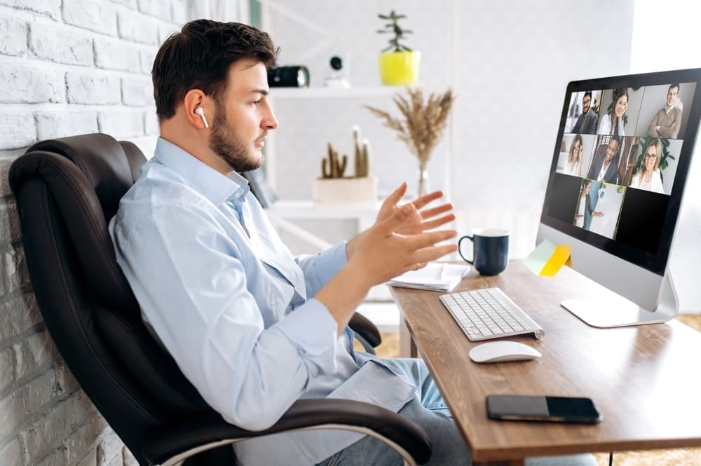 A staff member taking a video call with colleagues at their desk, wearing wireless earbuds